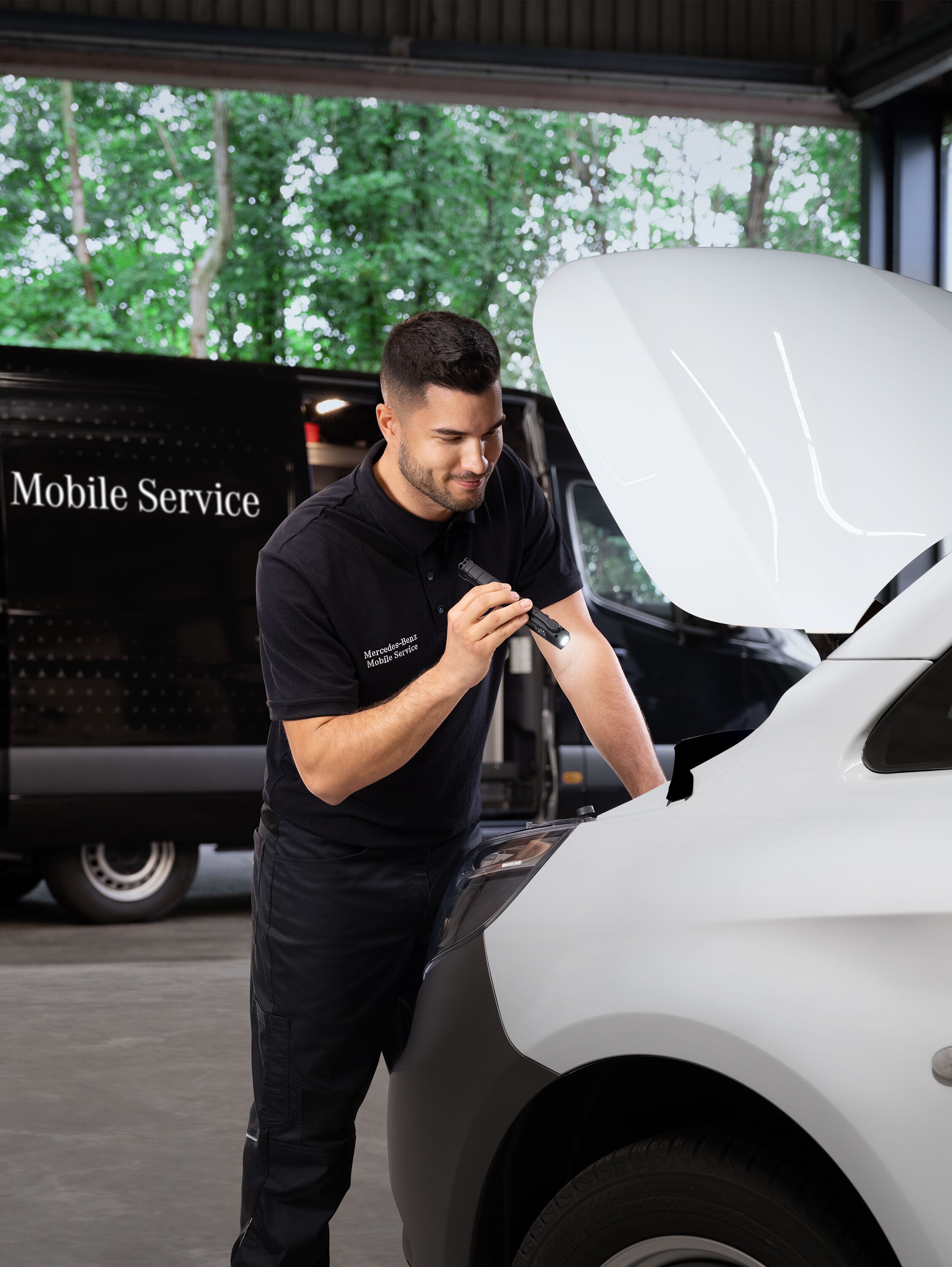 Mecánico inspeccionando el motor de un furgón Mercedes-Benz blanco.