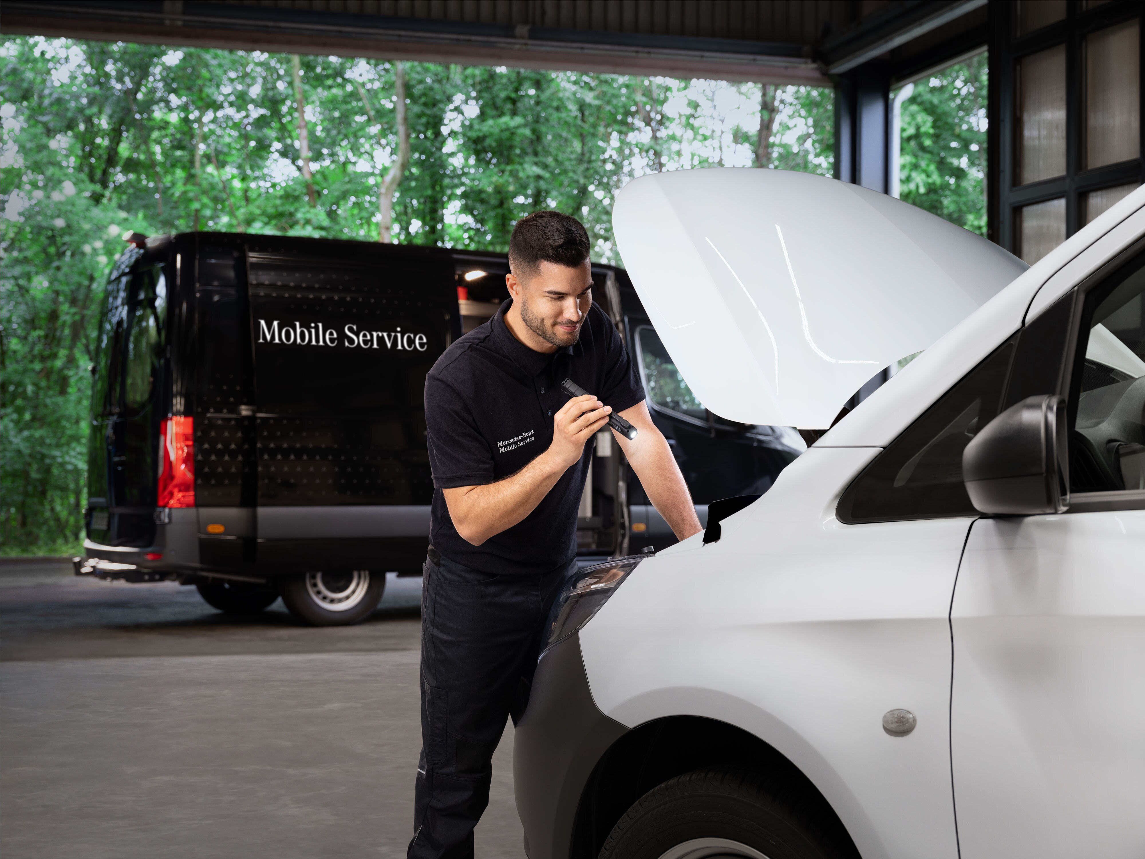 Mecánico inspeccionando el motor de un furgón Mercedes-Benz blanco.