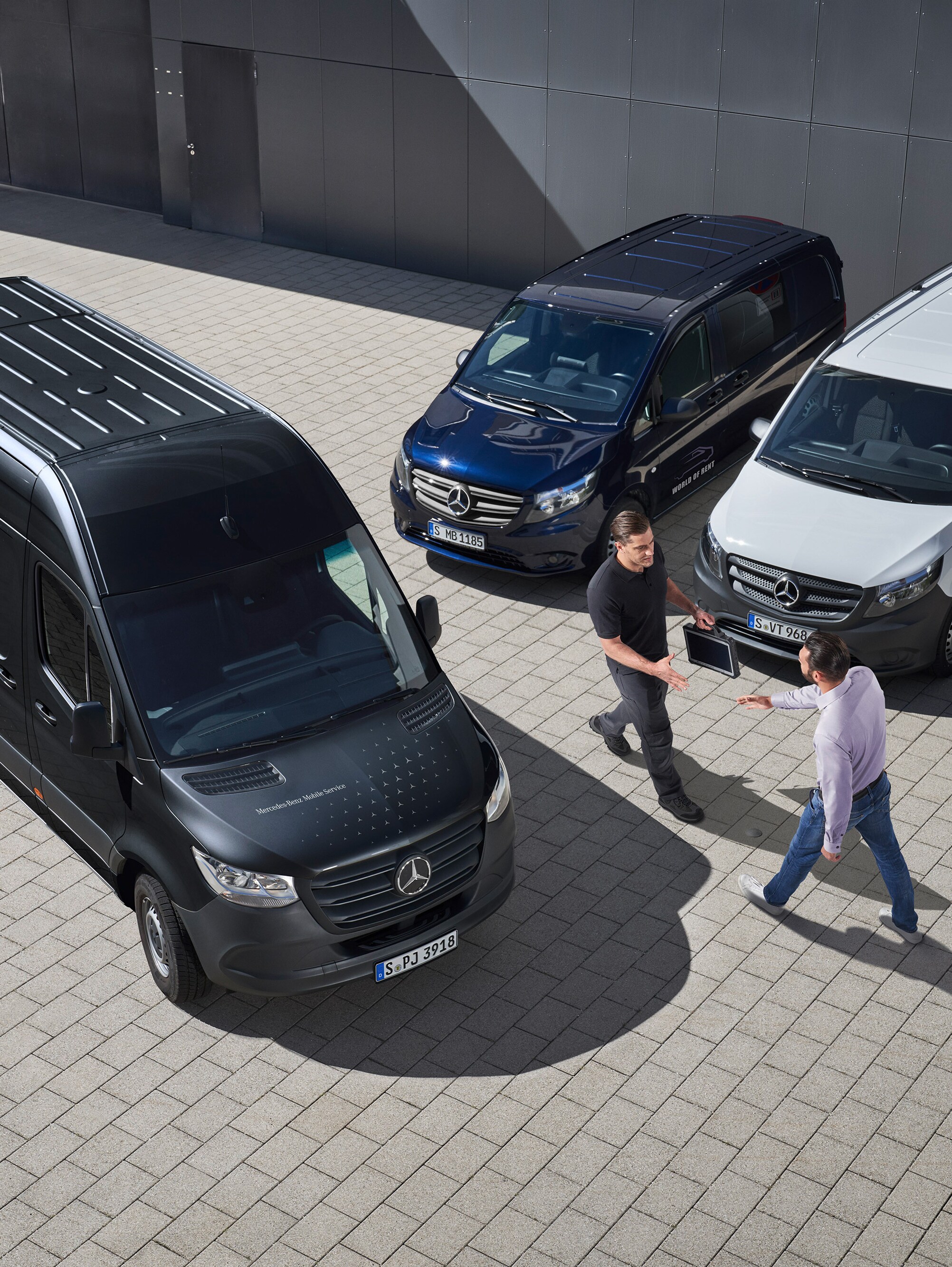 Dos hombres se saludan entre furgones Mercedes-Benz.