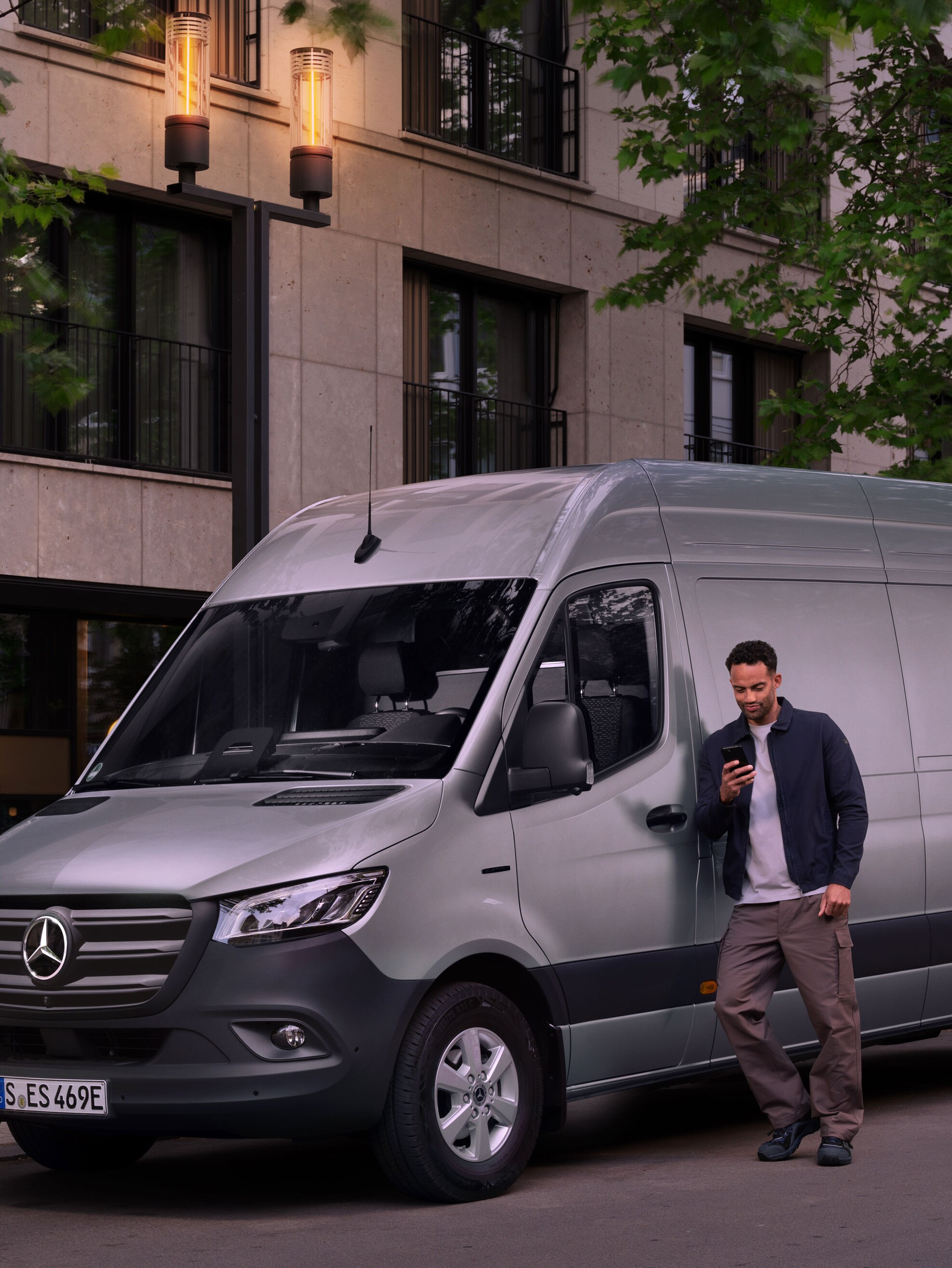 Hombre completando un informe de daños en su teléfono móvil, apoyado en un Mercedes-Benz Sprinter plateado.