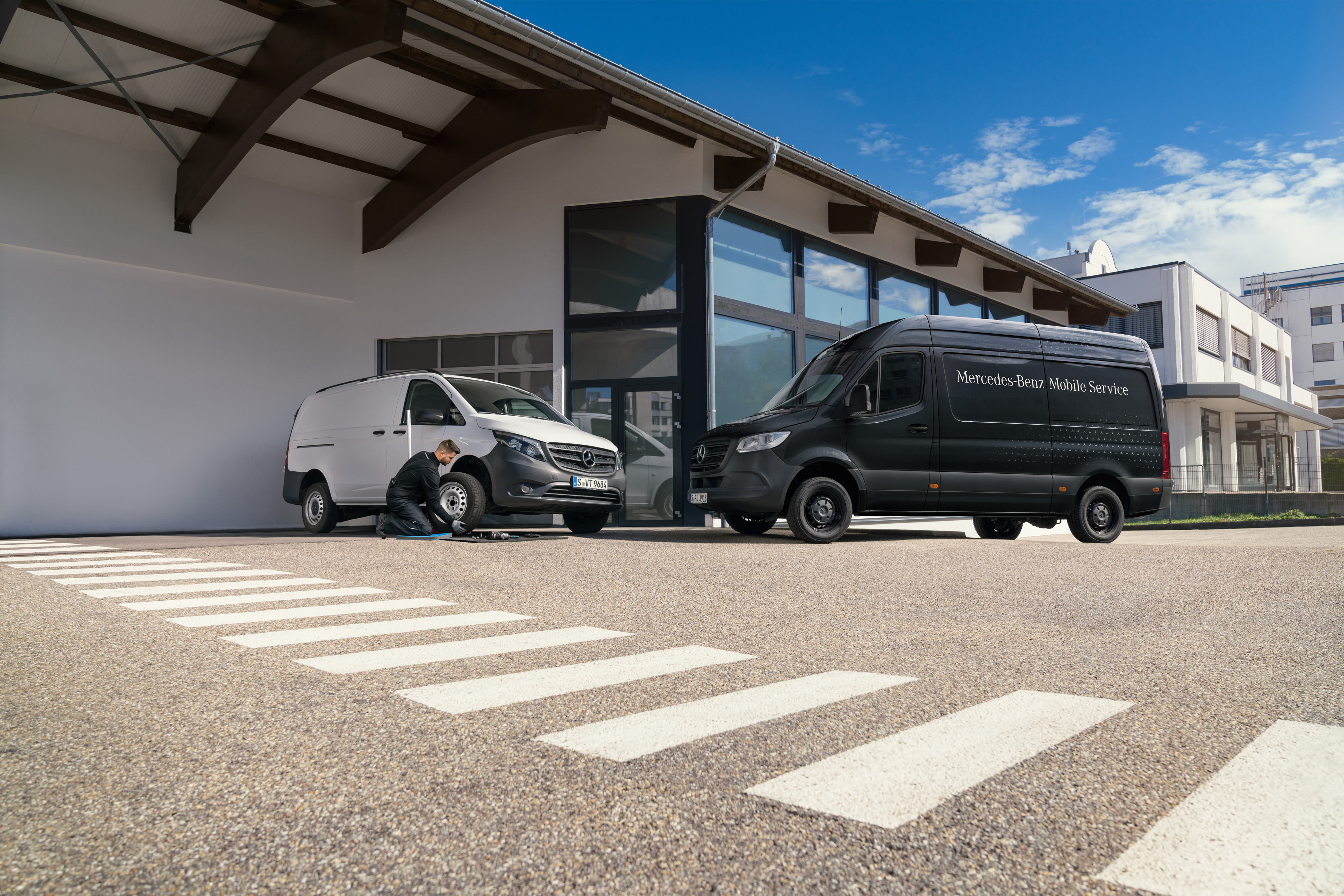 Mercedes-Benz | Servicio móvil | Sistema de frenos Un técnico cambiando un neumático de un furgón Mercedes-Benz Vito blanco delante de una sala de exposiciones.