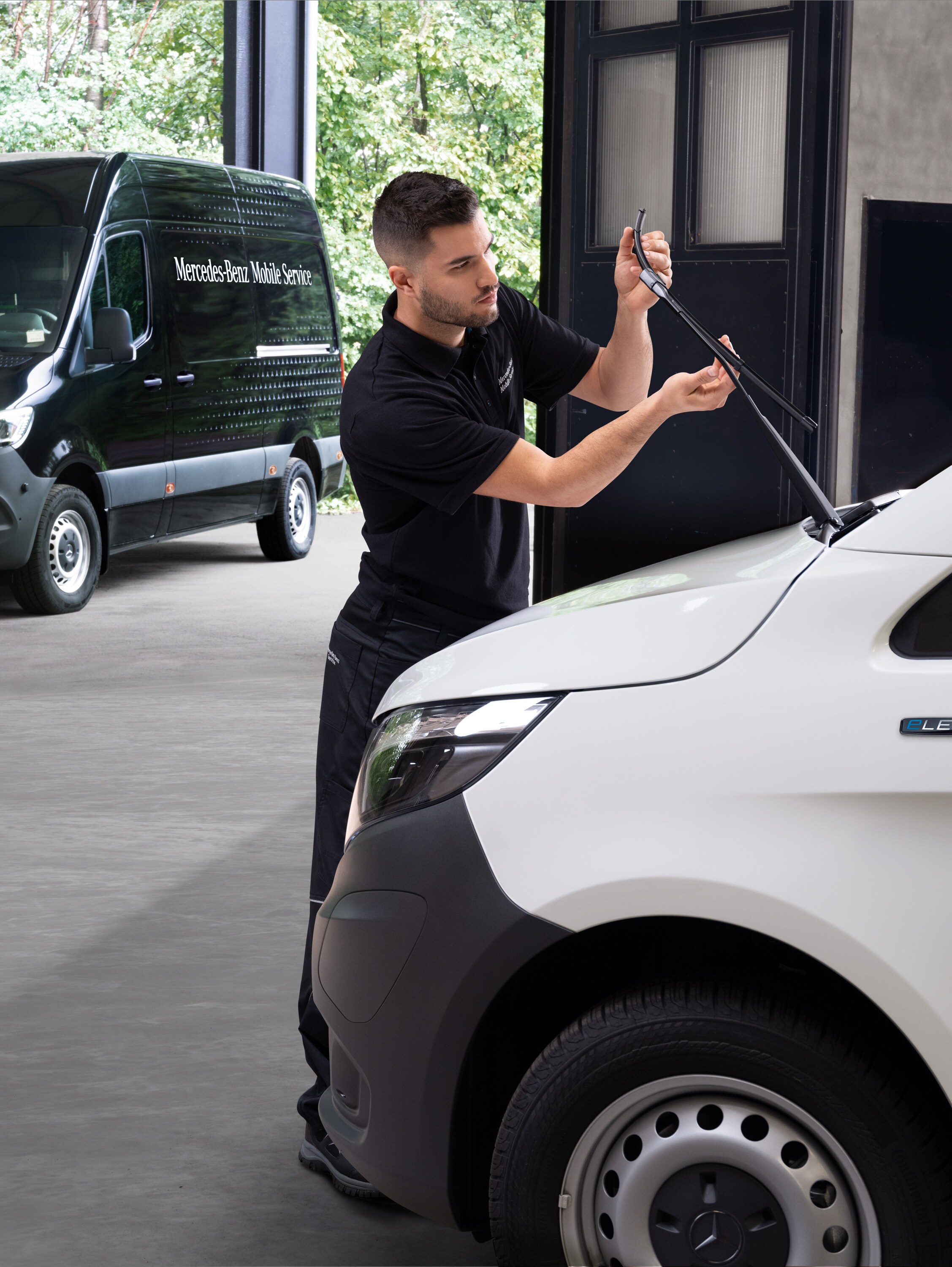 Un técnico cambiando las escobillas limpiaparabrisas de un furgón Mercedes-Benz Vito blanco.