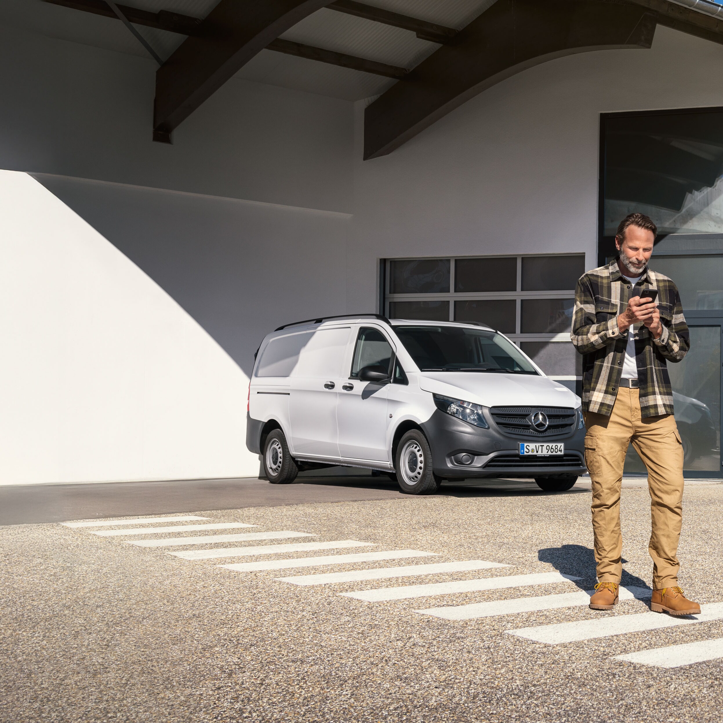 Un cliente, parado delante de un furgón Mercedes-Benz Vito de color blanco, reservando una cita usando su dispositivo móvil.
