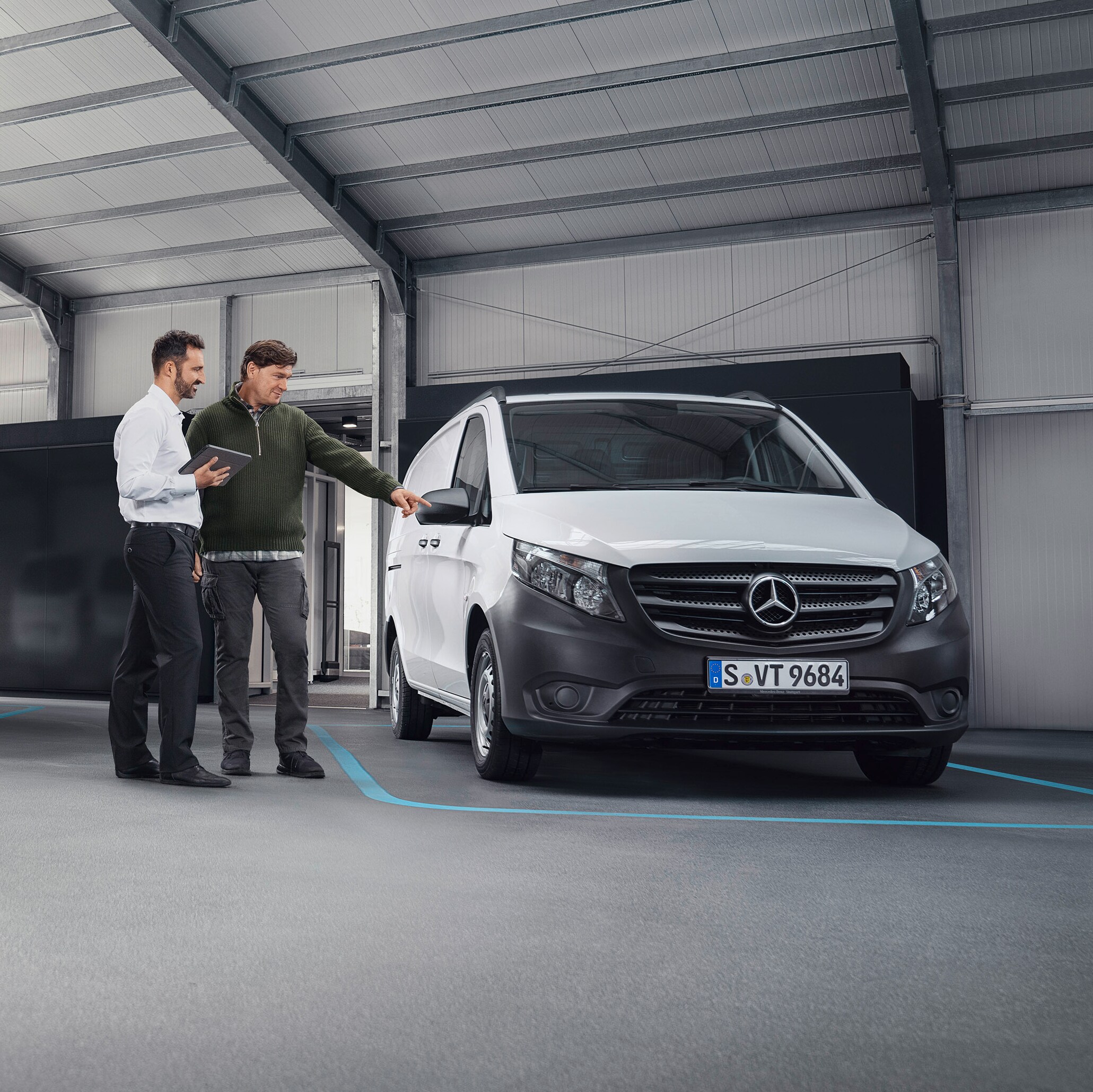 Agente de atención al cliente de Mercedes-Benz con un cliente en un punto de servicio asociado delante de un furgón.
