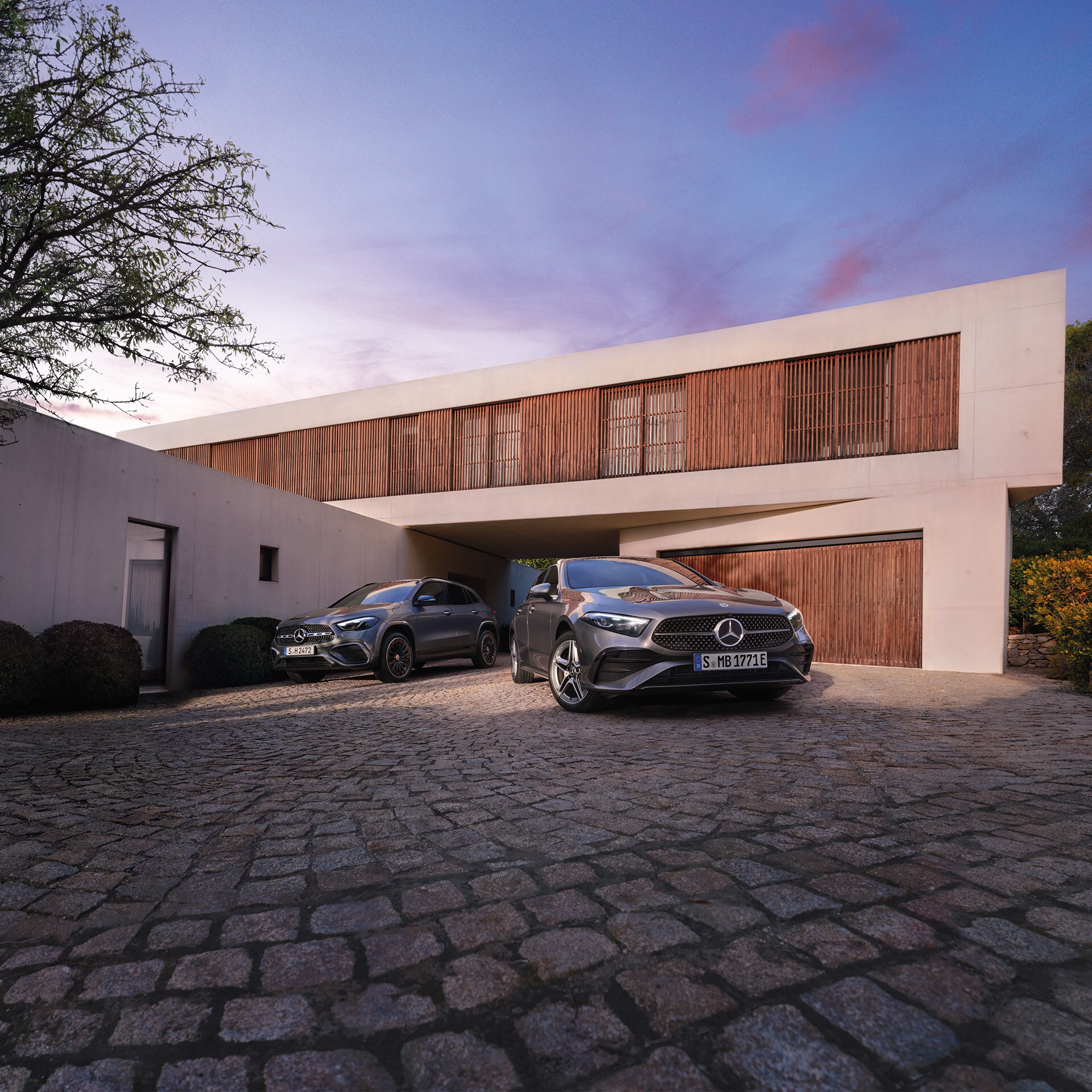 visual frontal de un Clase y un GLA de color negro aparcados enfrente de una casa