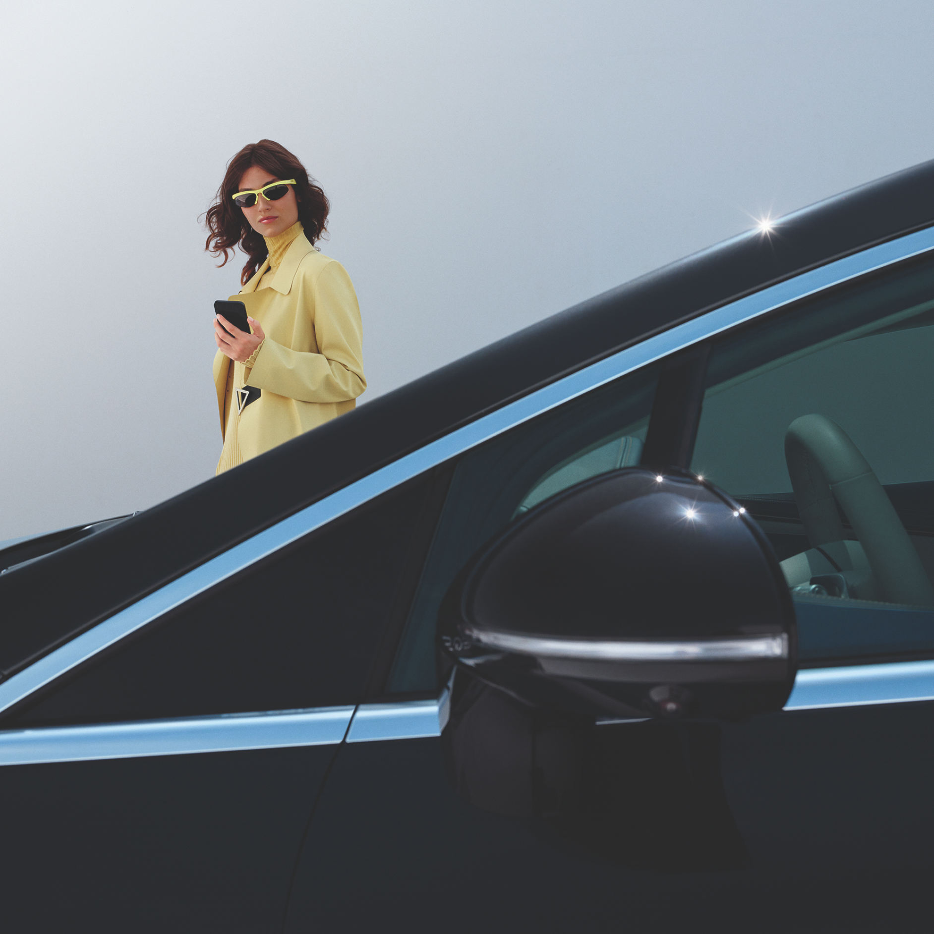 Mercedes-Benz | Oferta Cambio de Lunas visual de una mujer vestida de amarillo con gafas de sol detrás de un coche negro