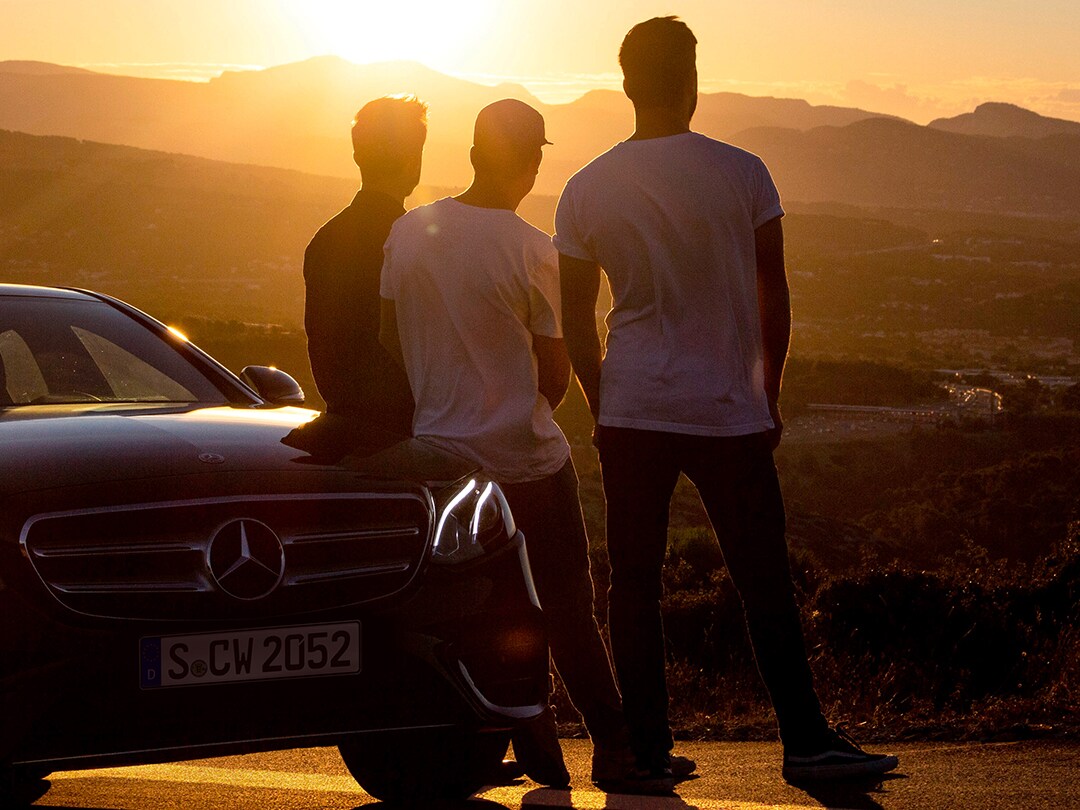 Vista de tres hombres de espalda mirando el atardecer, apoyados en un Mercedes-Benz