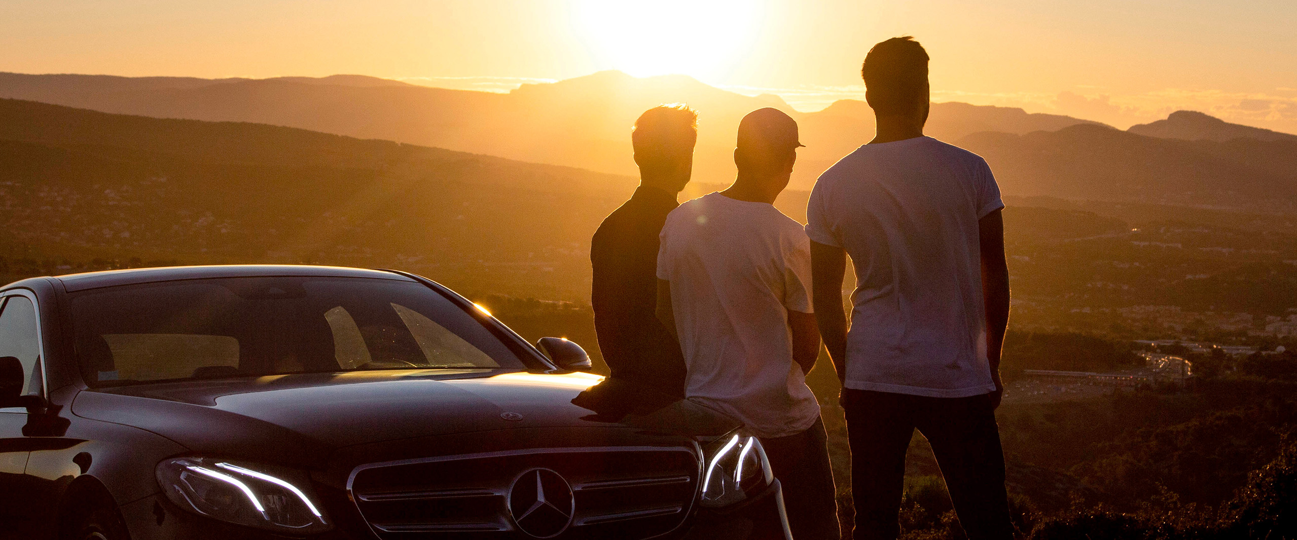 140 años de innovación | Mercedes-Benz Vista de tres hombres de espalda mirando el atardecer, apoyados en un Mercedes-Benz