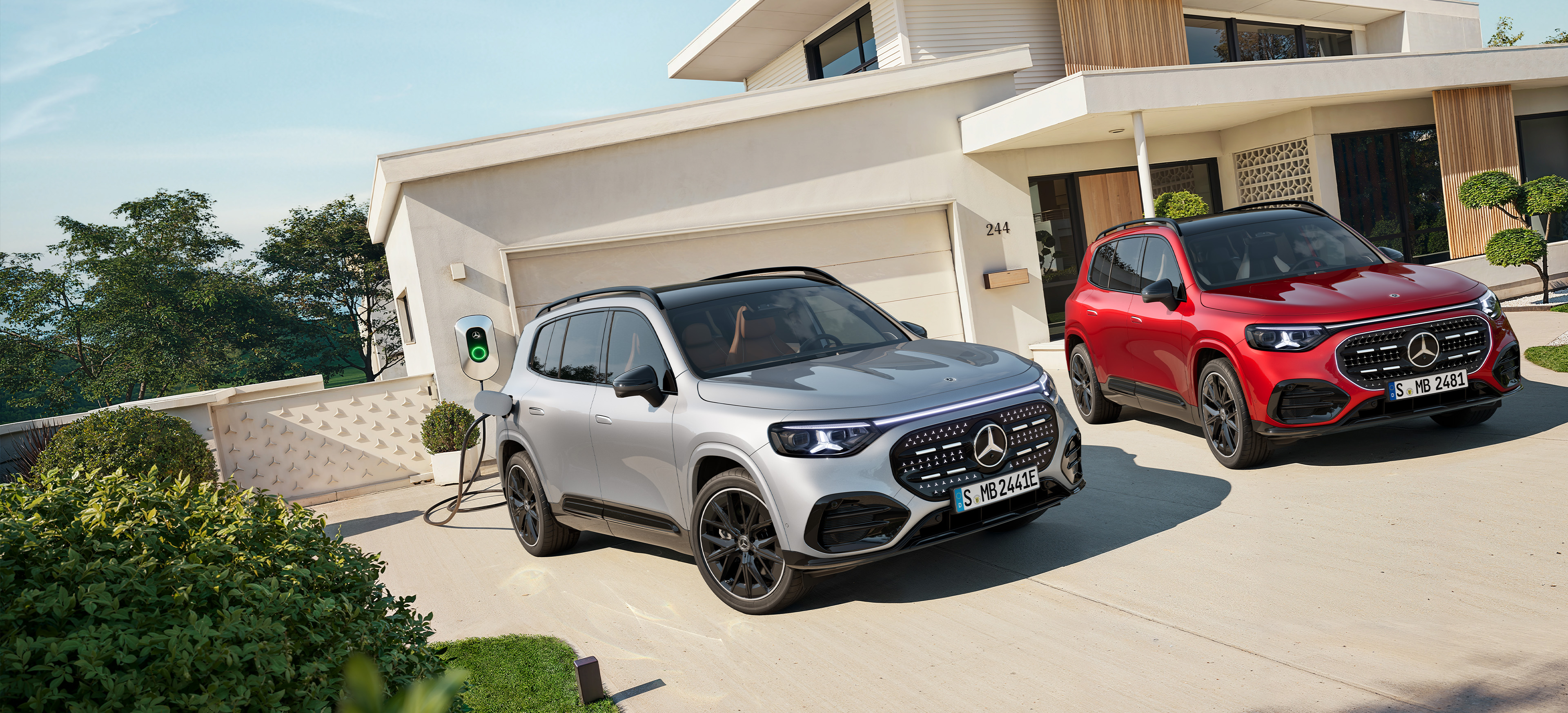 Nuevo GLB | Mercedes-Benz El nuevo GLB eléctrico en rojo y gris aparcados fuera de una casa