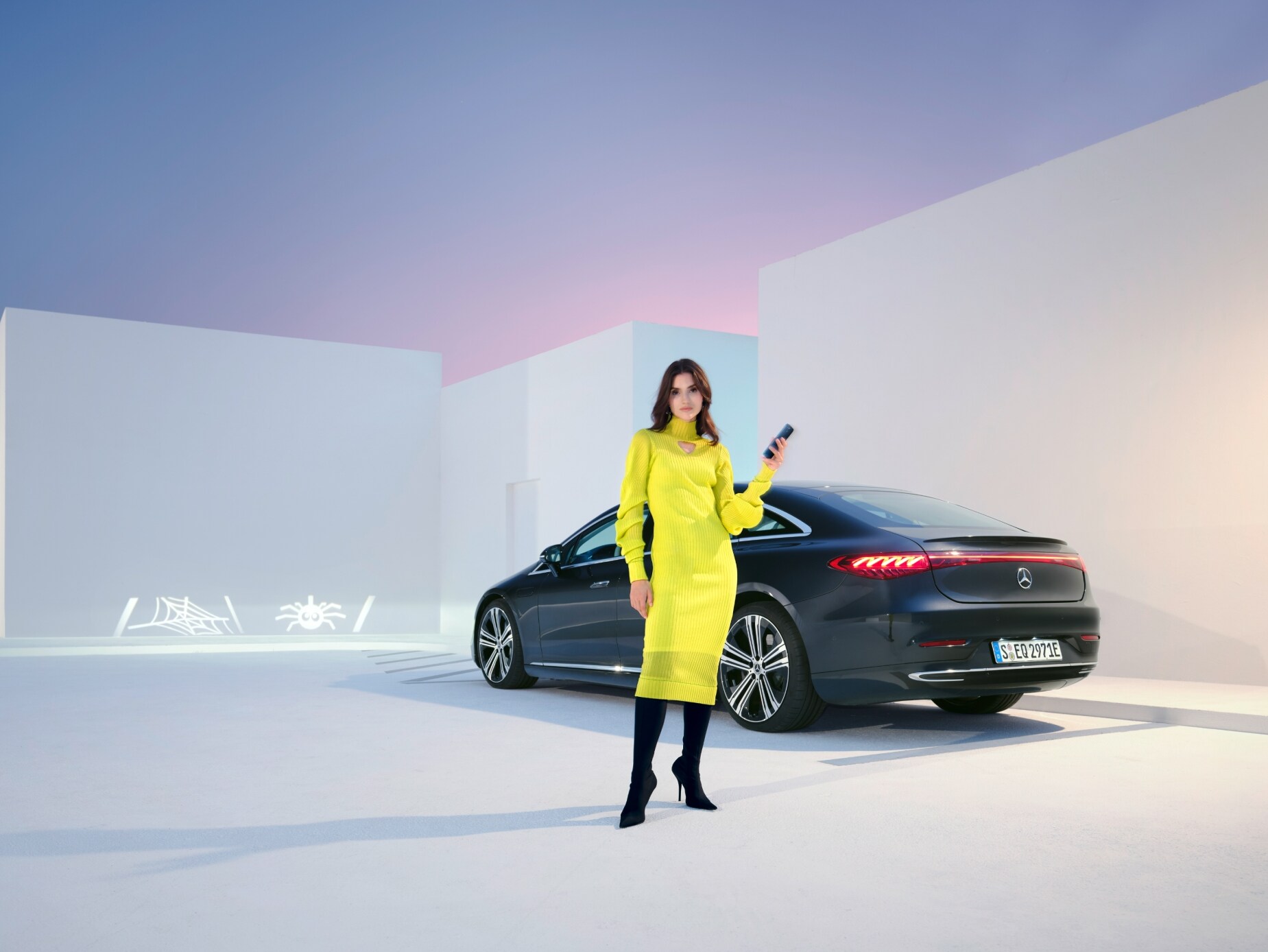 visual de una mujer vestida de amarillo con gafas de sol detrás de un coche negro