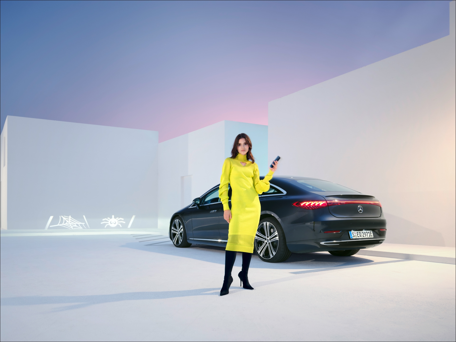 Extras Digitales | Mercedes-Benz visual de una mujer vestida de amarillo con gafas de sol detrás de un coche negro