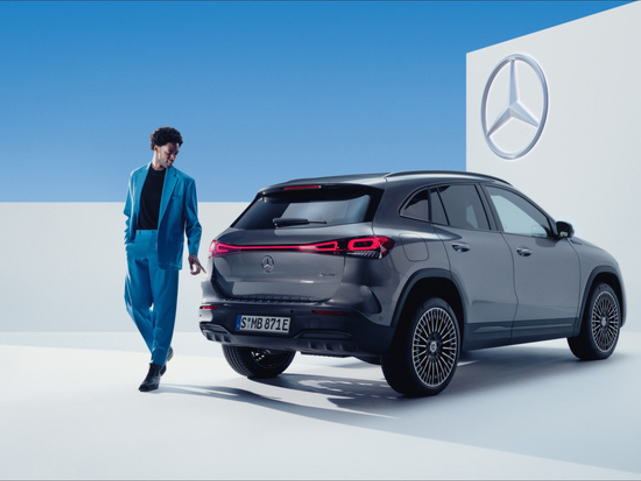 Un hombre con un traje azul detras de un EQ negro de Mercedes-Benz