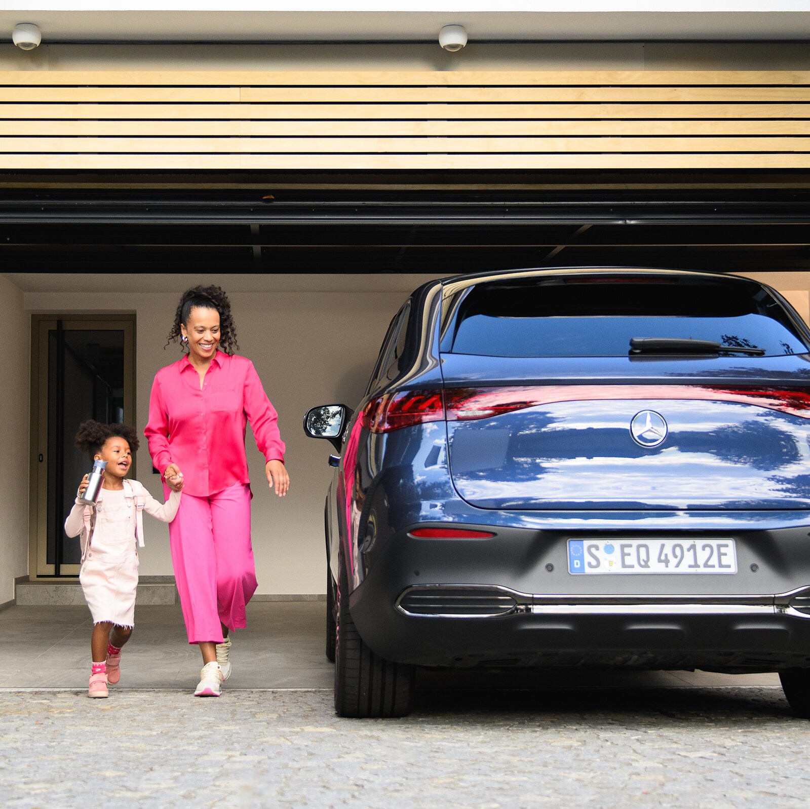 Una niña y una mujer delante de un EQE SUV de Mercedes-Benz.