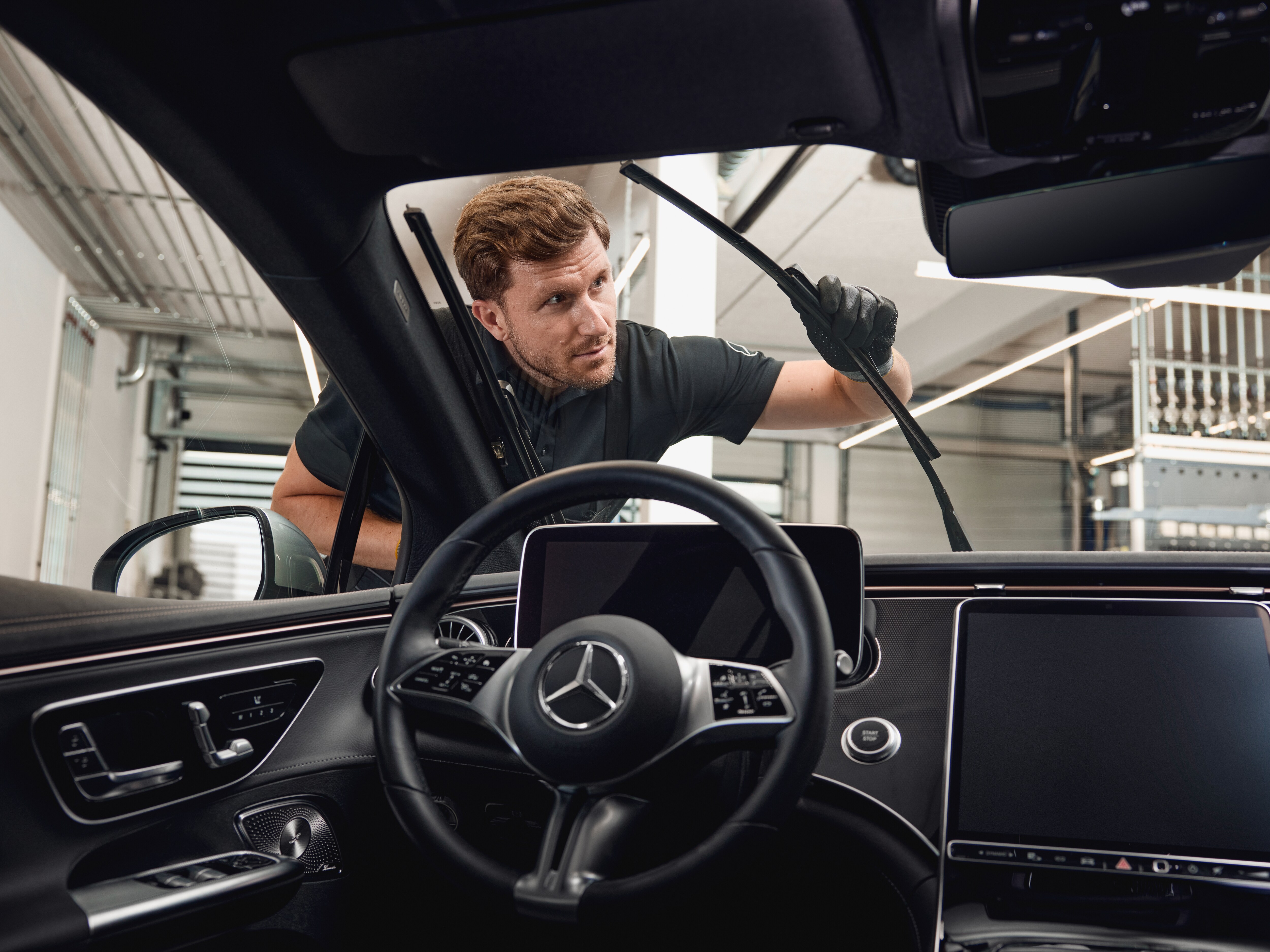 Vista interior de un vehículo Mercedes-Benz con un técnico cambiando escobillas limpiaparabrisas originales.