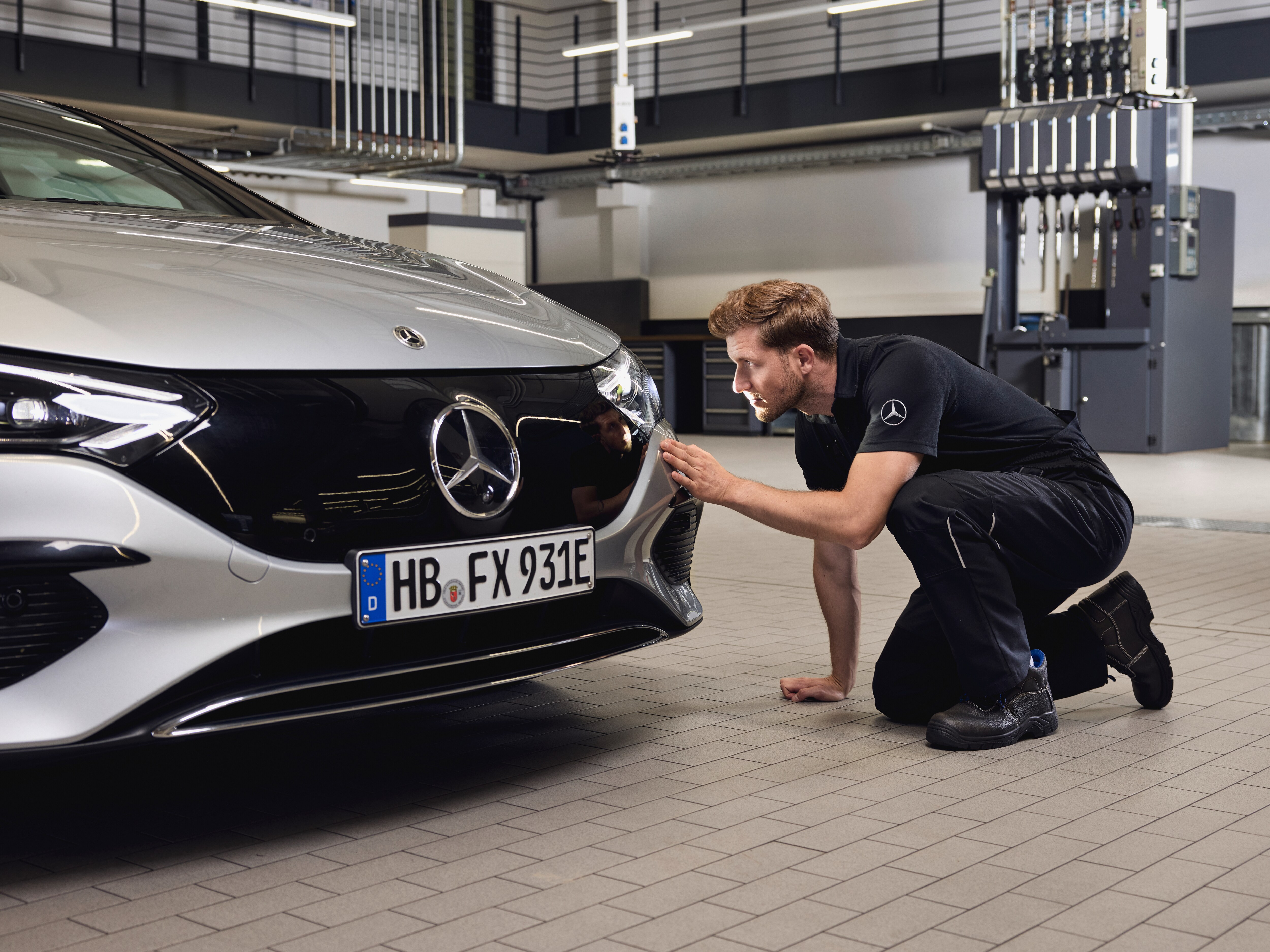 Primer plano de la parte delantera de un vehículo Mercedes-Benz con un técnico realizando un examen detallado sobre la sustitución de piezas originales Mercedes-Benz.