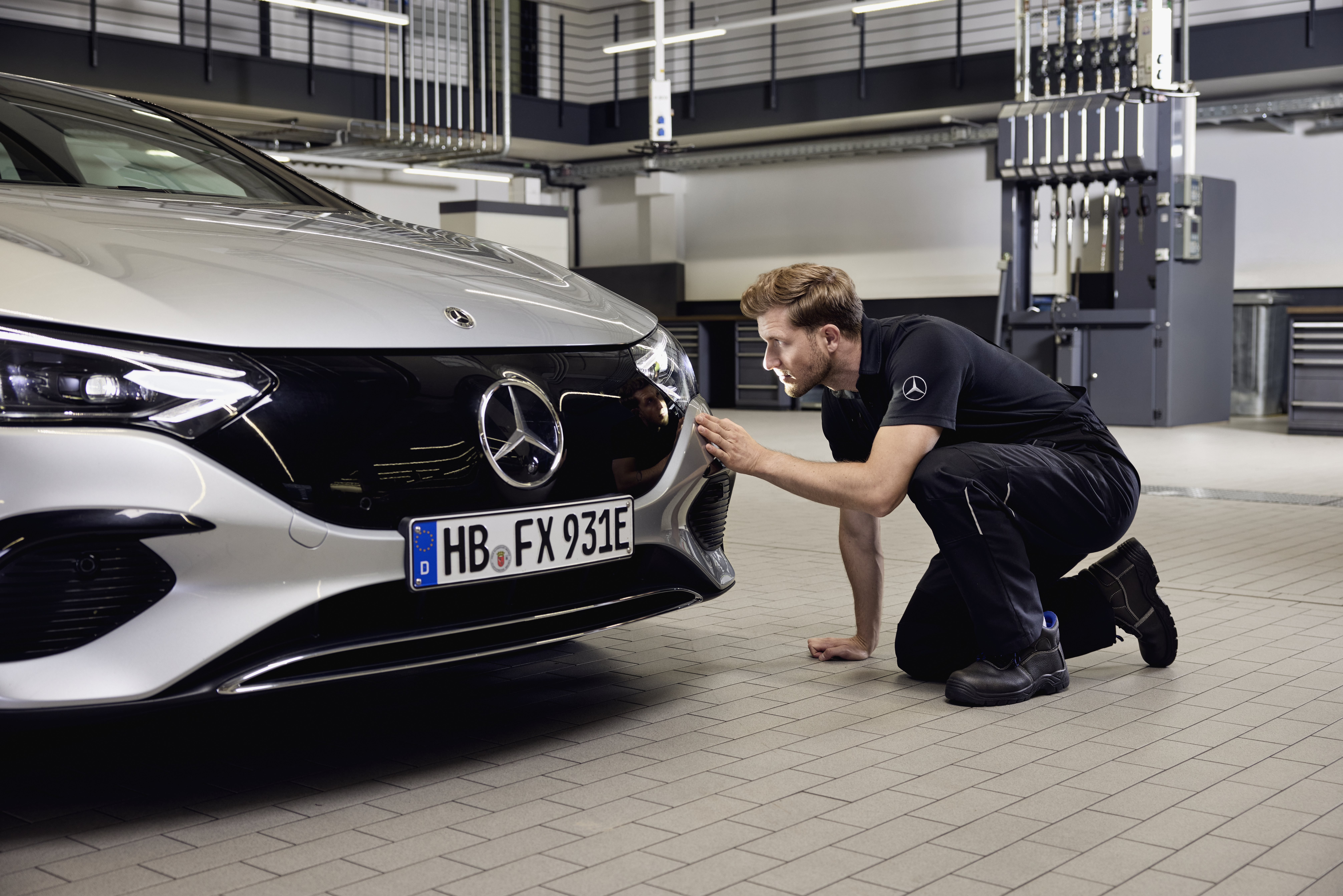 Sustitución de faros originales Mercedes-Benz Primer plano de la parte delantera de un vehículo Mercedes-Benz con un técnico realizando un examen detallado sobre la sustitución de piezas originales Mercedes-Benz.