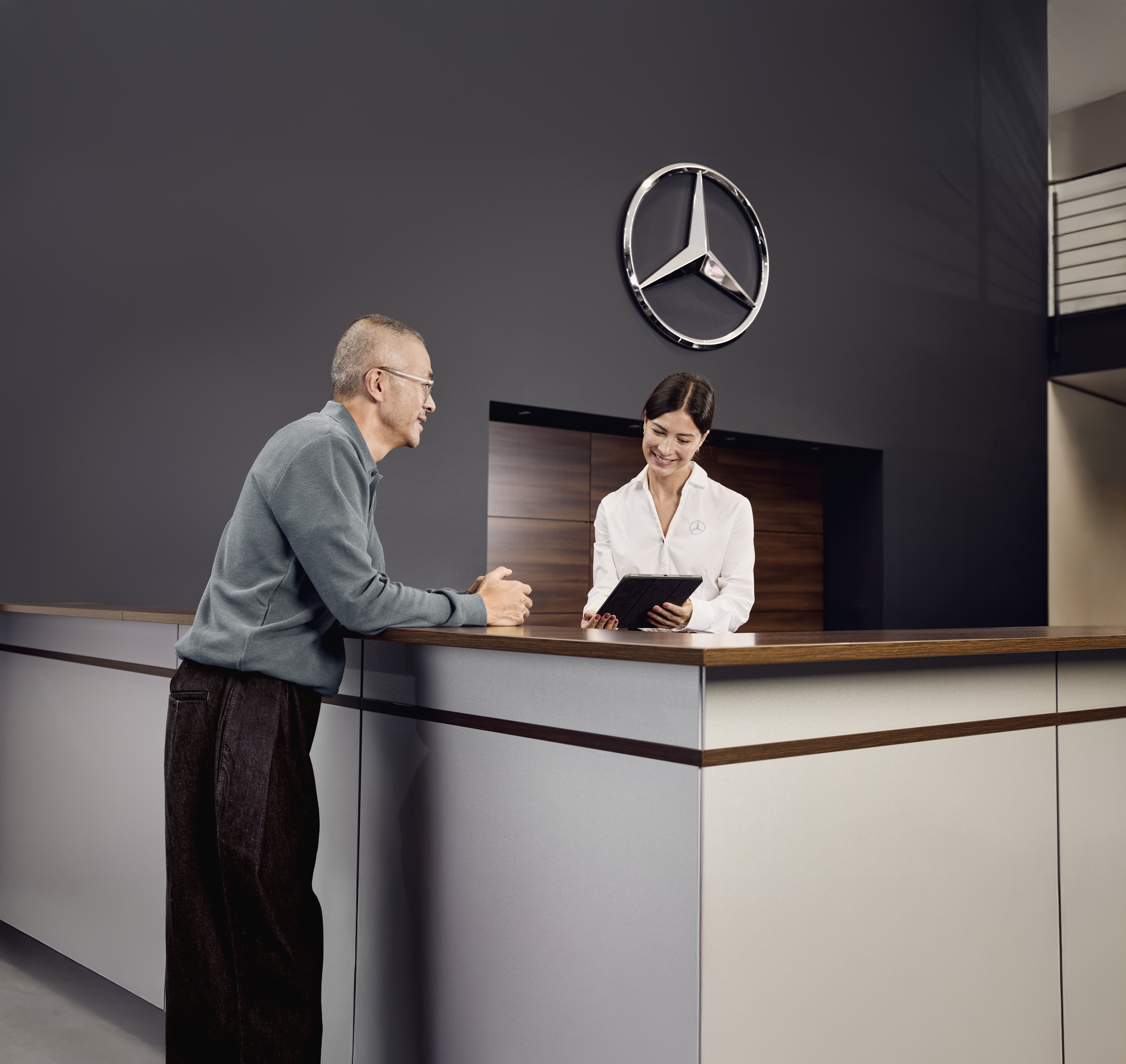 Consulta por recambios originales Mercedes-Benz Área de recepción de servicios en un concesionario Mercedes-Benz; un cliente comentando los detalles del servicio de su vehículo con un asesor de servicios en la recepción.
