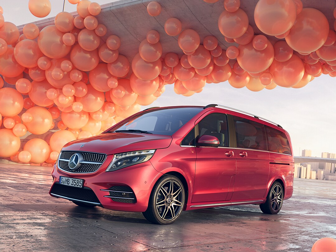 Monovolumen premium Mercedes-Benz Clase V en color rojo posicionado en un escenario urbano moderno con elementos decorativos