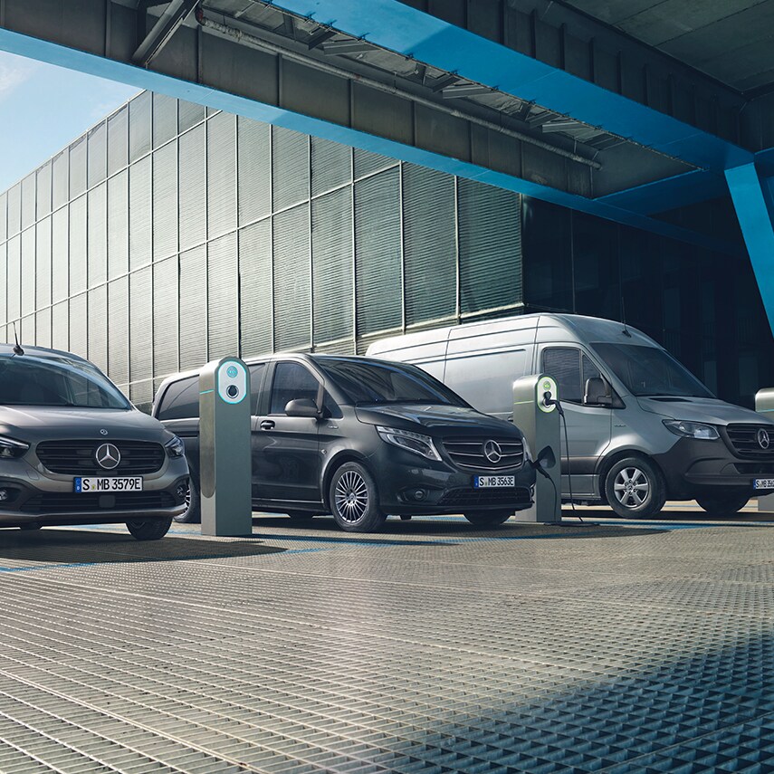 Tres Mercedes eléctricas cargando en una instalación industrial moderna con puntos de recarga, bajo una estructura futurista, representando la movilidad sostenible y la logística urbana eléctrica.