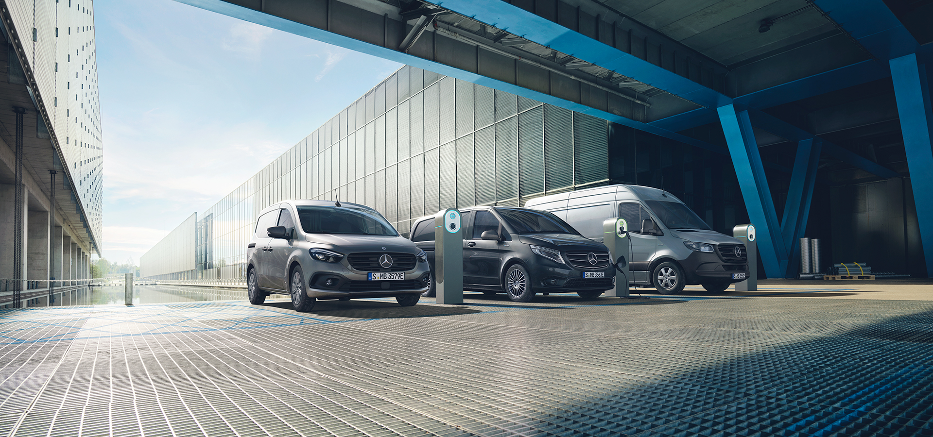 Tres Mercedes eléctricas cargando en una instalación industrial moderna con puntos de recarga, bajo una estructura futurista, representando la movilidad sostenible y la logística urbana eléctrica.
