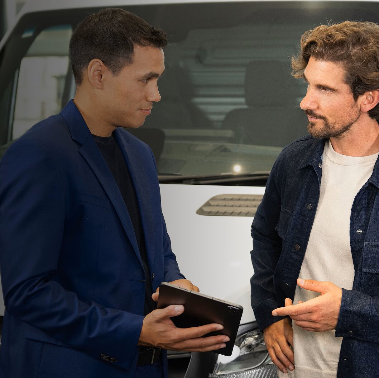 Asesor de Mercedes-Benz mostrando información en una tablet a un cliente junto a una Sprinter en un concesionario.