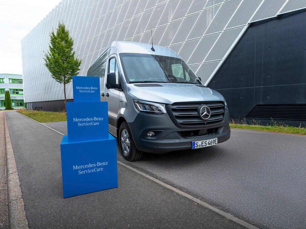 Mercedes-Benz eSprinter estacionada frente a un edificio moderno junto a elementos promocionales de Mercedes-Benz ServiceCare, destacando las soluciones de mantenimiento y servicio para vehículos comerciales.