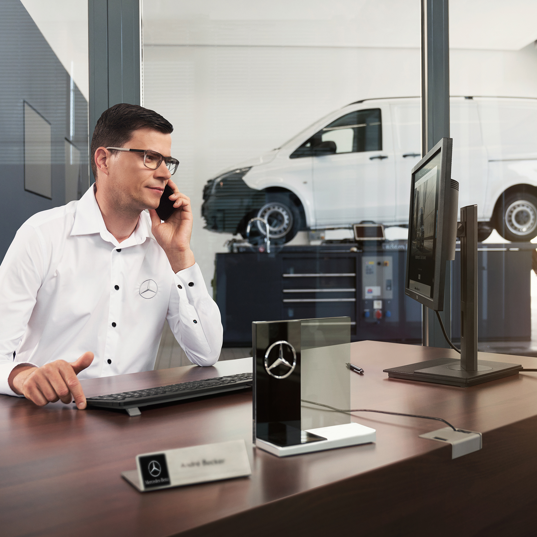 Seguros | Servicios financieros | Furgonetas Mercedes-Benz Un empleado de Mercedes-Benz atiende una llamada en un taller con una furgoneta elevándose.