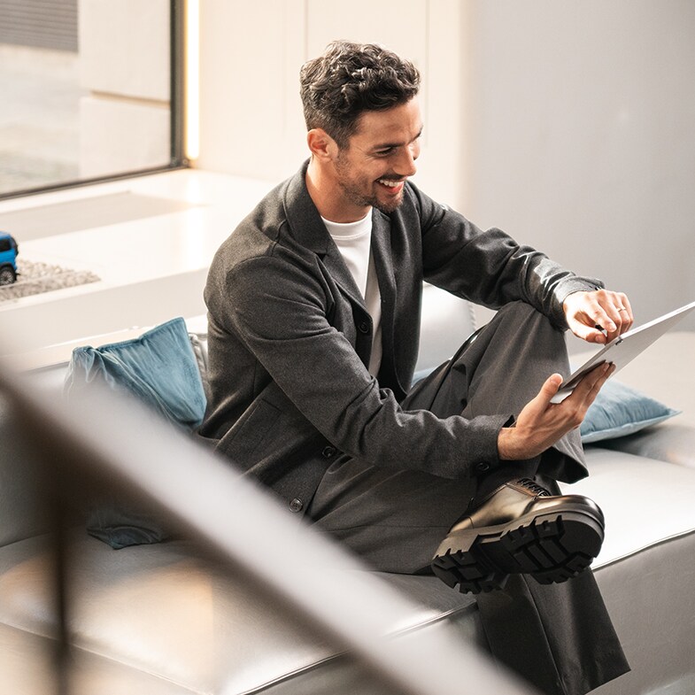 Un hombre sonríe mientras usa una tableta en un sofá.