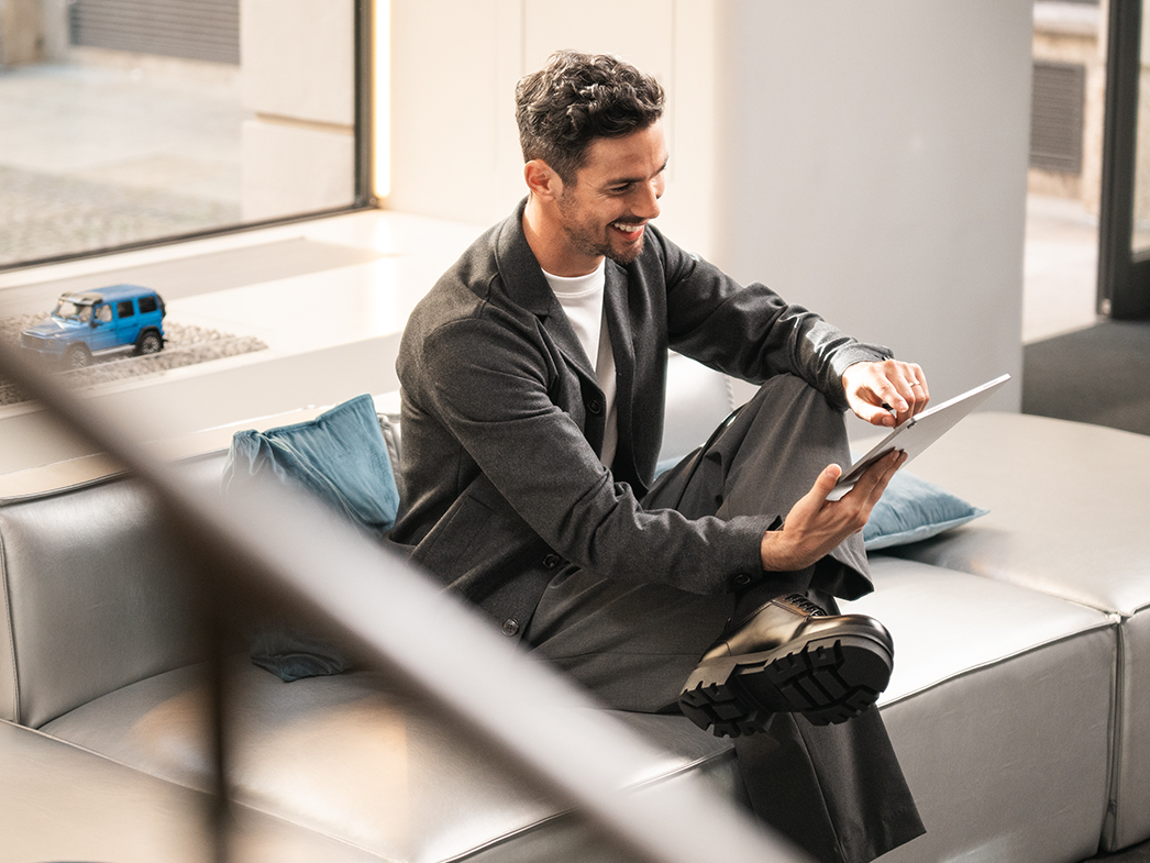 Portal del cliente | Servicios financieros | Furgonetas Mercedes-Benz Un hombre sonríe mientras usa una tableta en un sofá.